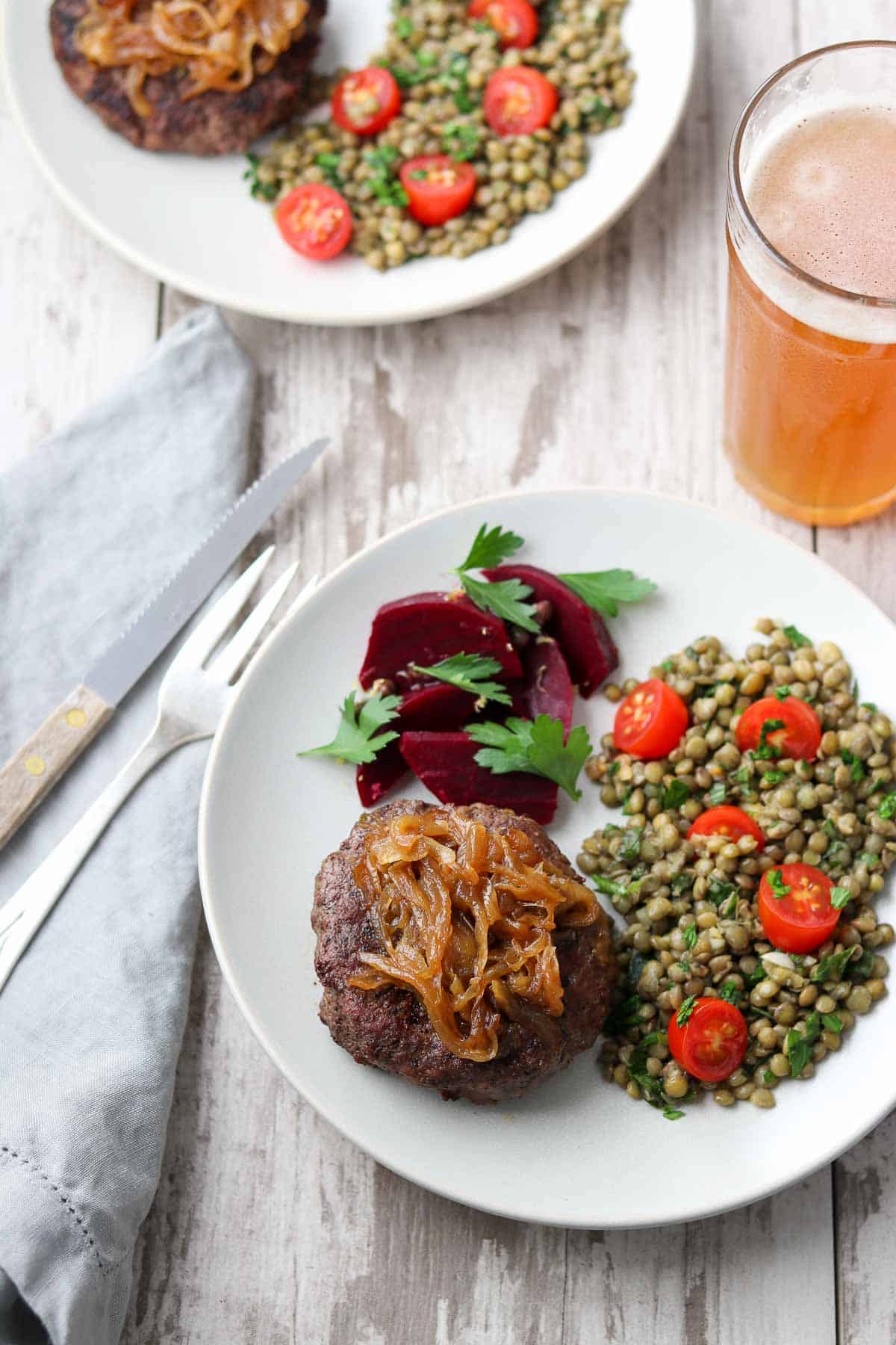 Burger topped with caramelized onions next to roasted beets and lentil salad.