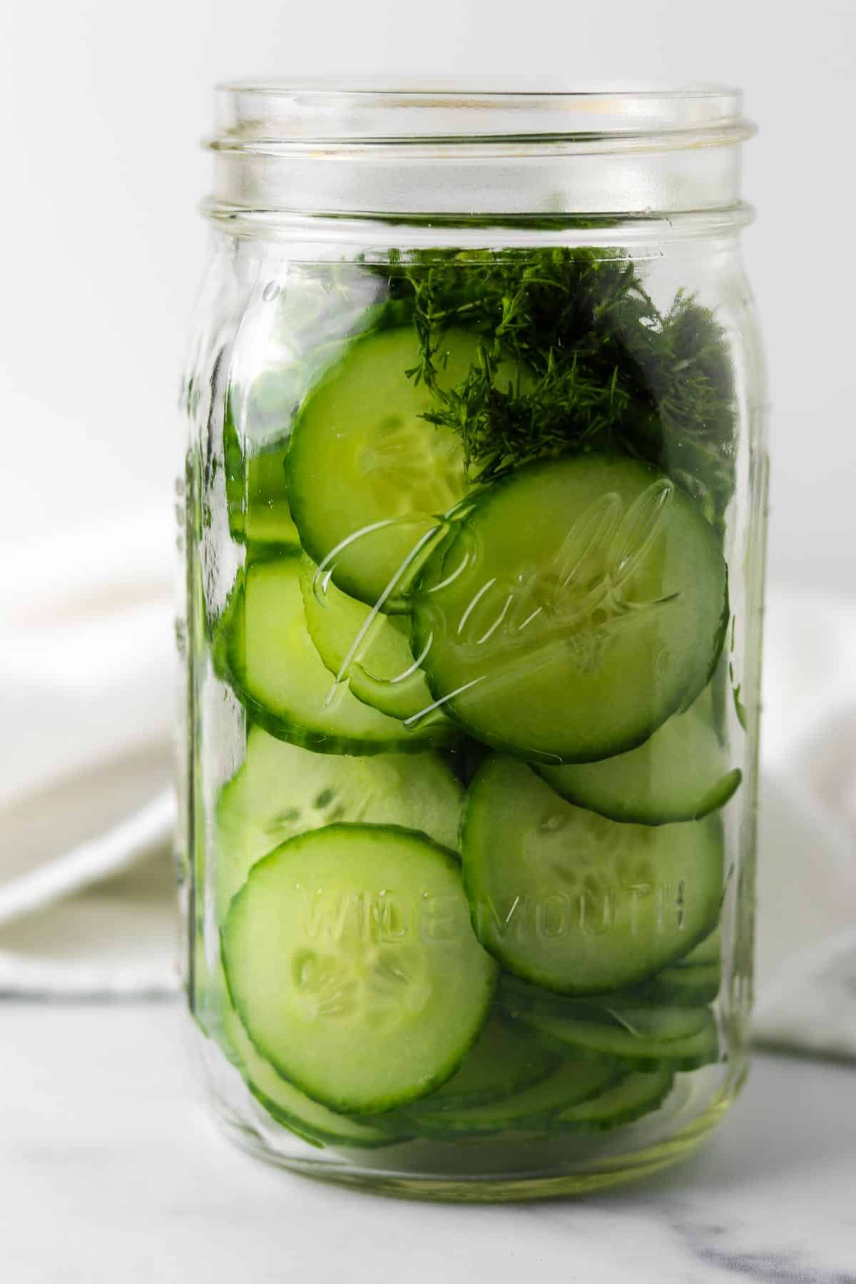 Sliced cucumbers and chopped dill in a jar.