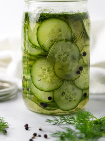Quick Swedish Pickled Cucumbers in a jar next to peppercorns and fresh dill sprigs.