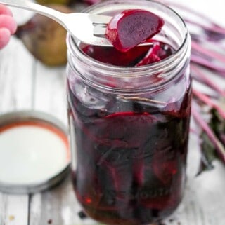 Pickled beets in a jar next to spices and beets.