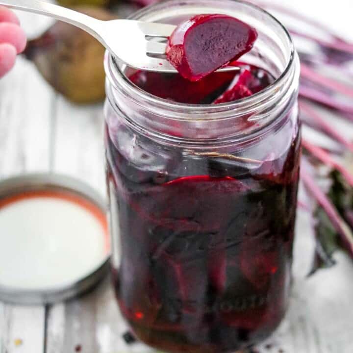 Pickled beets in a jar next to spices and beets.