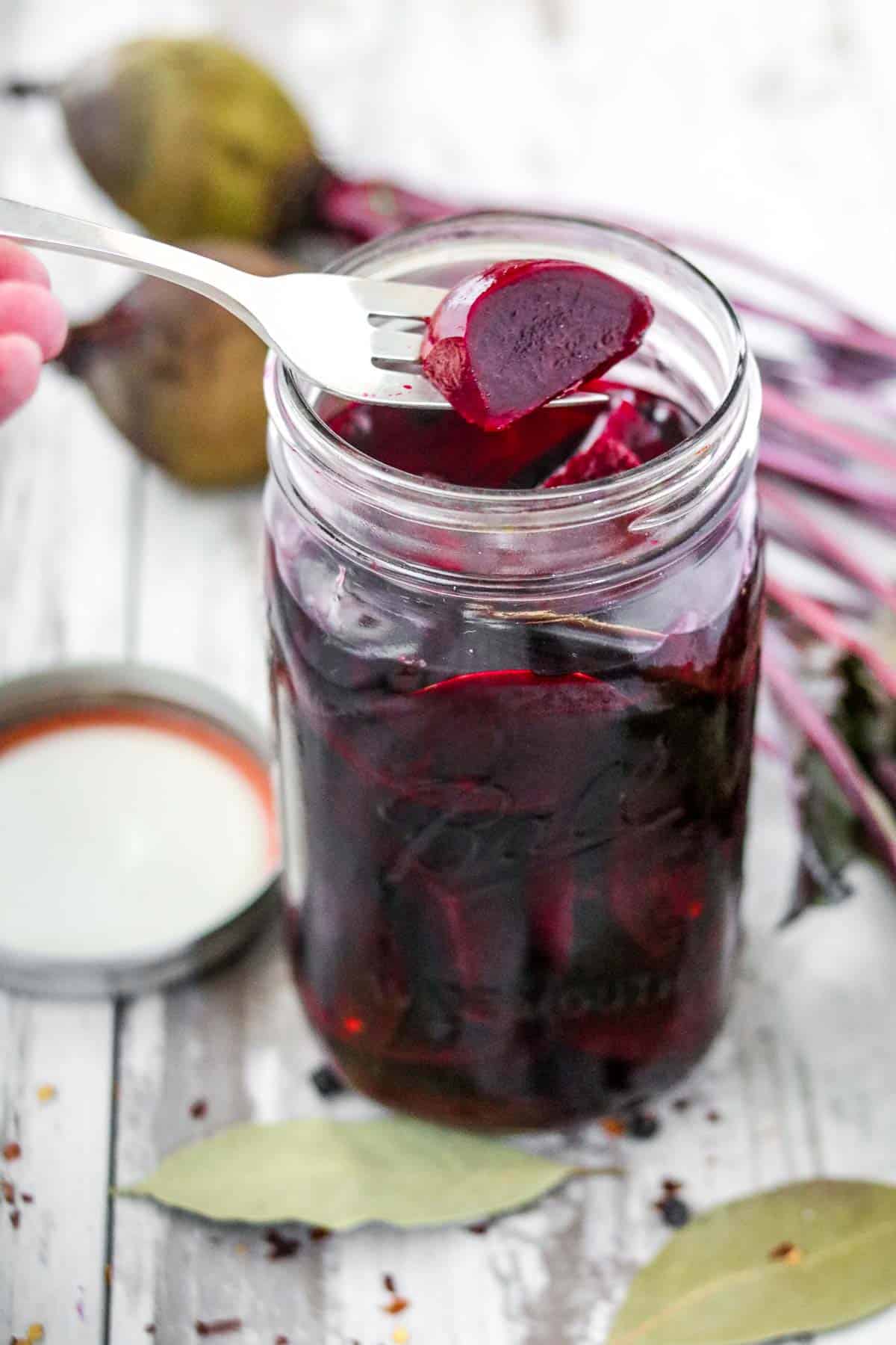 Pickled beets in a jar next to spices and beets.