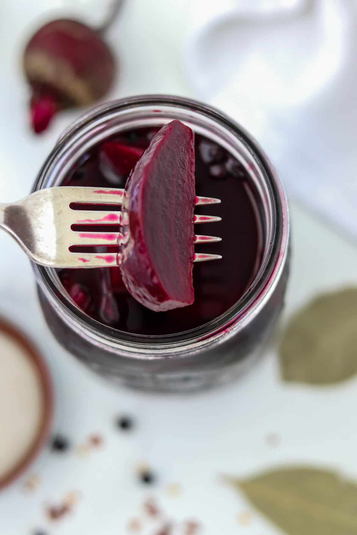 A pickled beet on a fork over a jar.