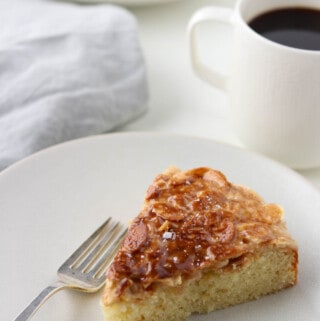 A slice of cake topped with caramelized onions next to a fork and a cup of coffee.