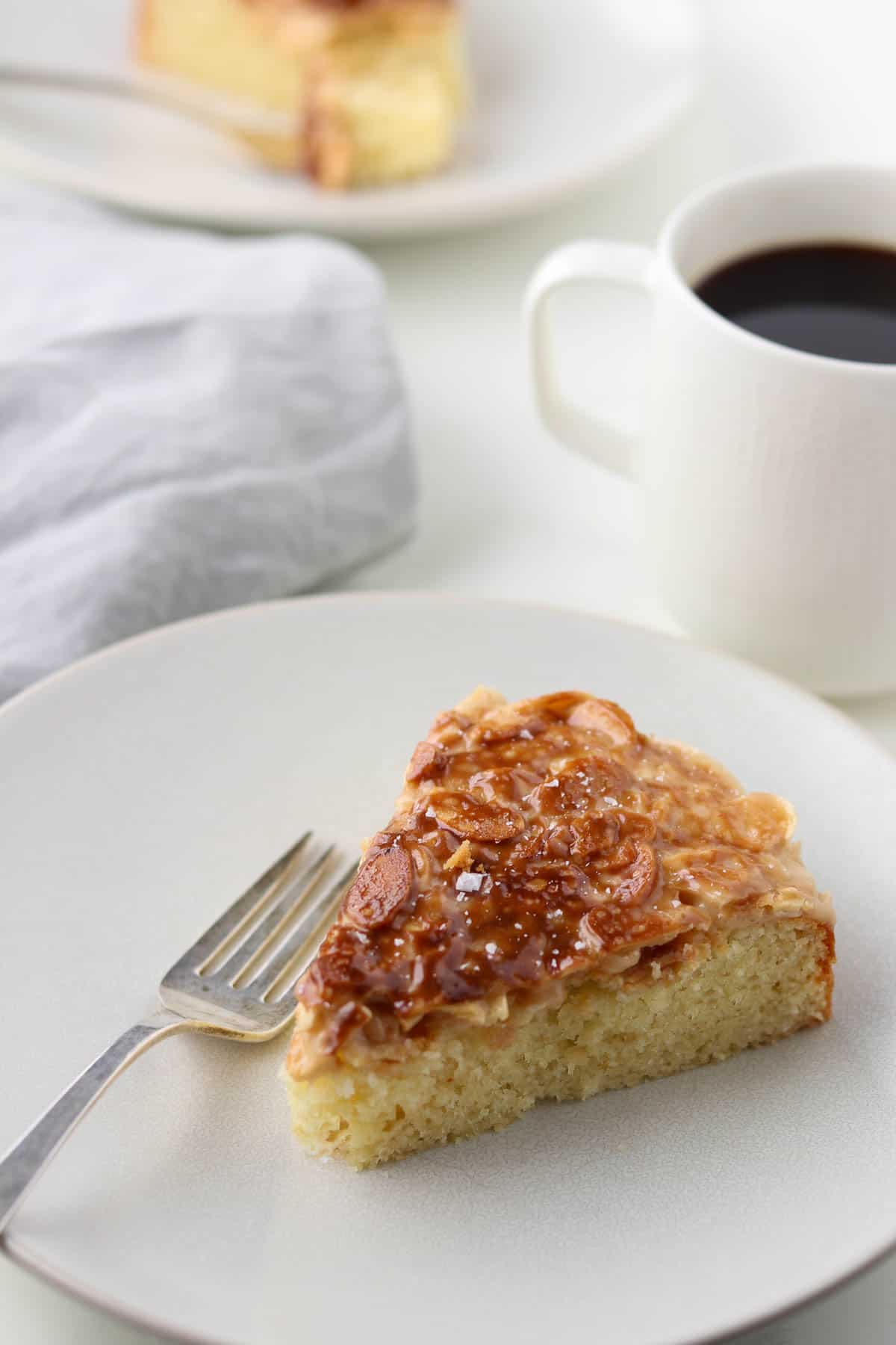 A slice of cake topped with caramelized onions next to a fork and a cup of coffee.