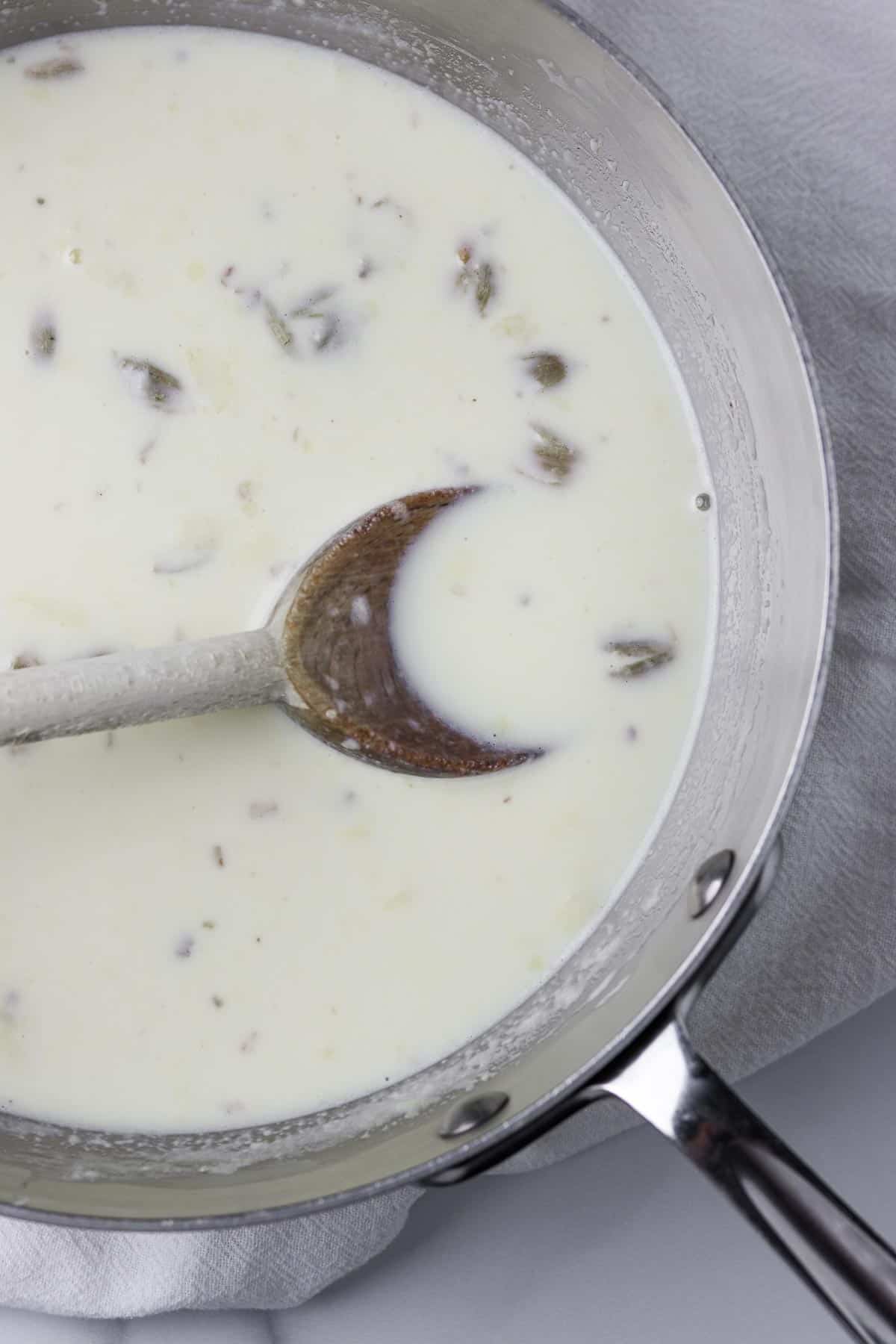 Cream, milk and cardamom pods in a saucepan with a wooden spoon.