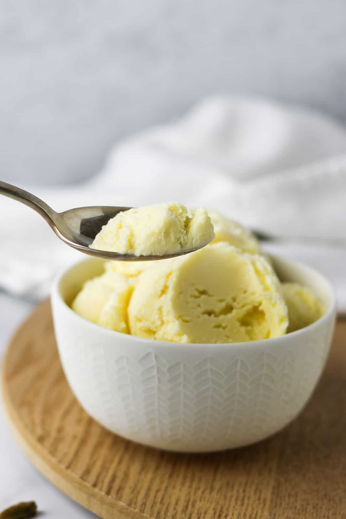 Cardamom Ice Cream in a bowl with a spoon on a wooden surface.