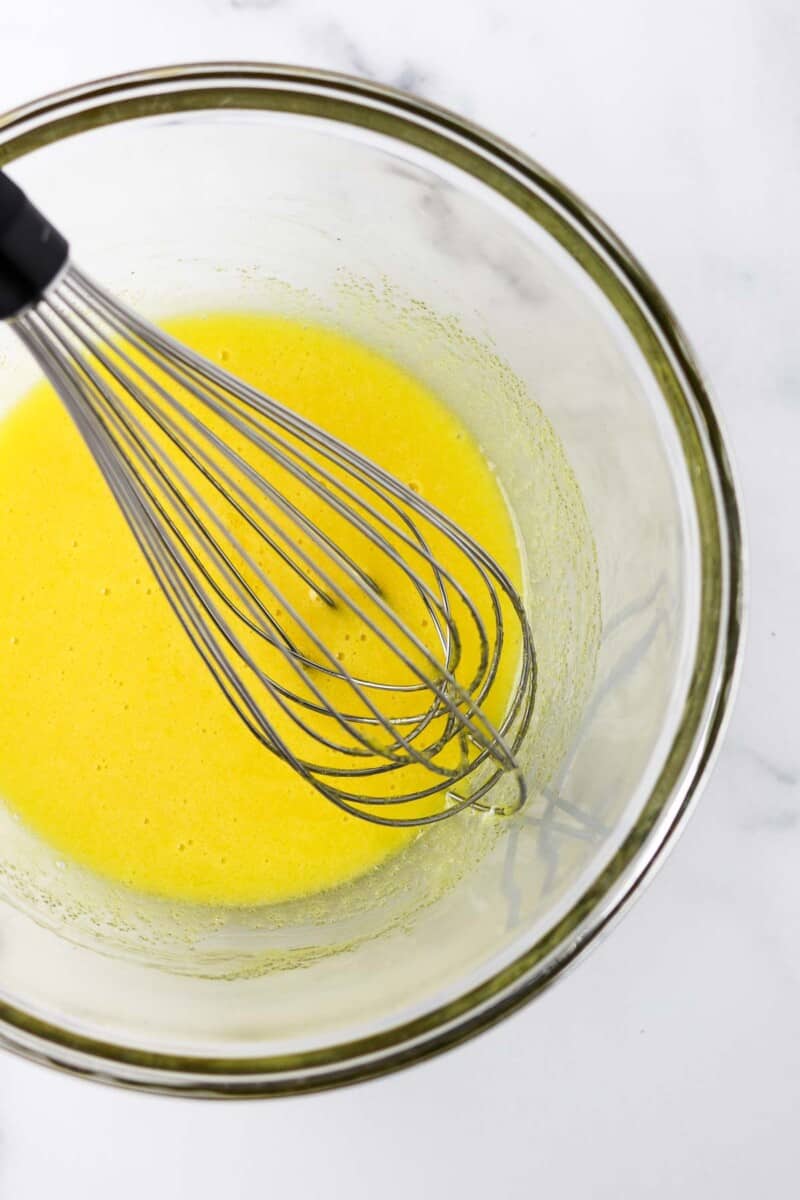 Egg yolks whisked together in a glass bowl with a whisk.