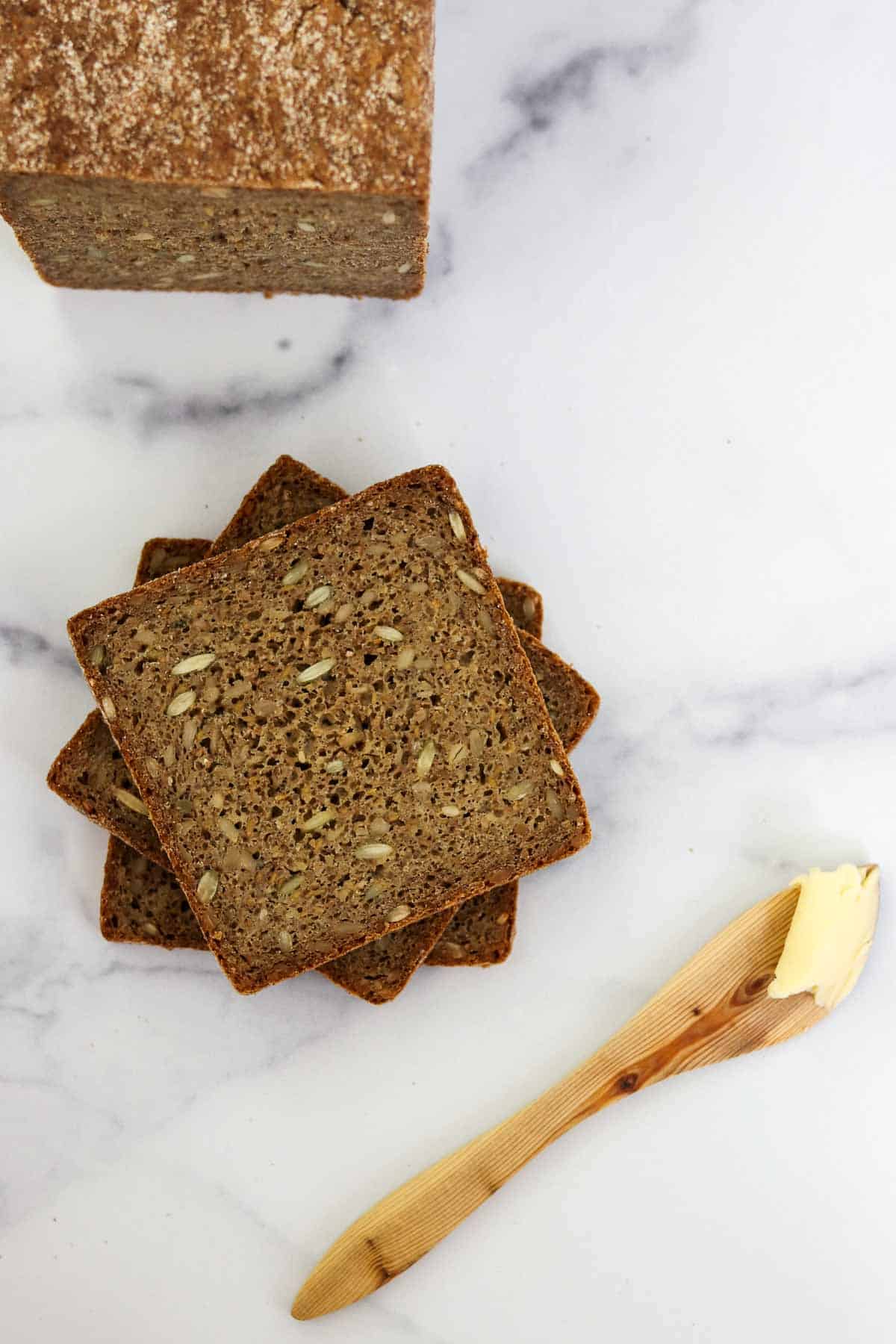 Slices of rye bread stacked on a marble surface next to a wooden butter knife.