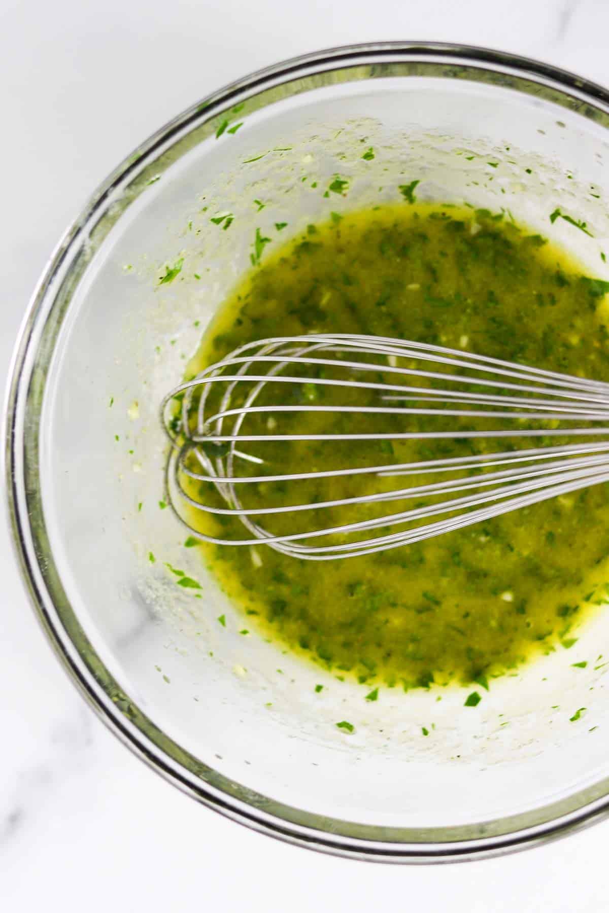 Herbed vinaigrette in a glass bowl with a whisk.