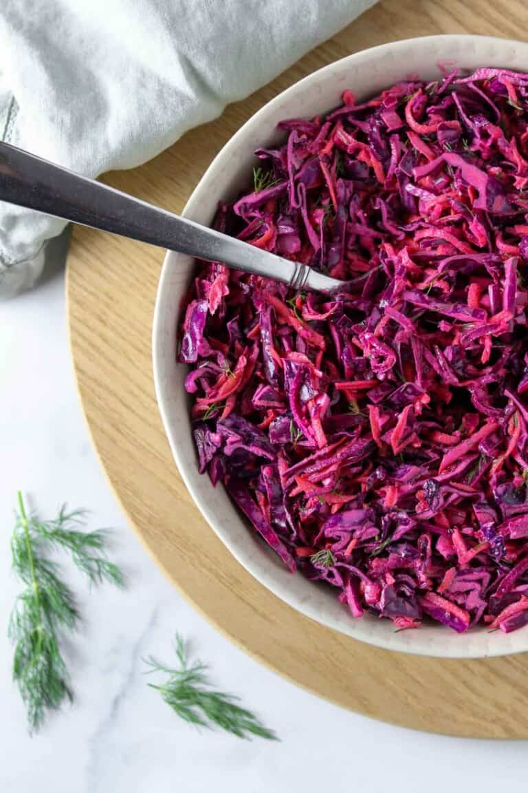 Red cabbage slaw in a bowl with a spoon on a wooden surface.