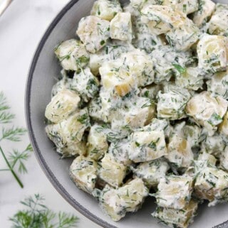 Creamy Herbed Potato Salad in a bowl next to a spoon and dill sprigs.