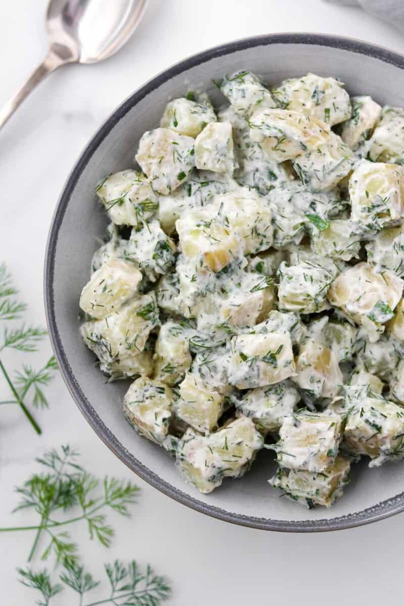 Creamy Herbed Potato Salad in a bowl next to a spoon and dill sprigs.