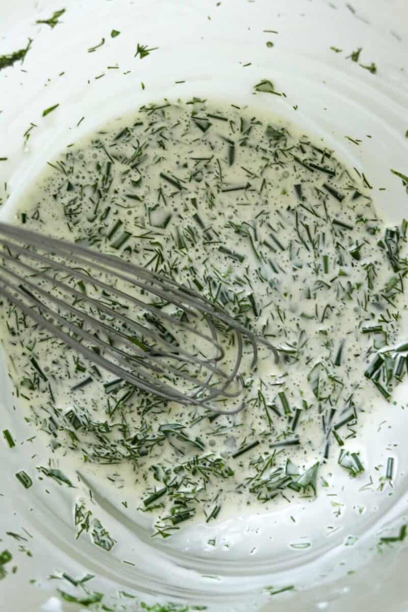 Creamy herb dressing in a bowl with a whisk.