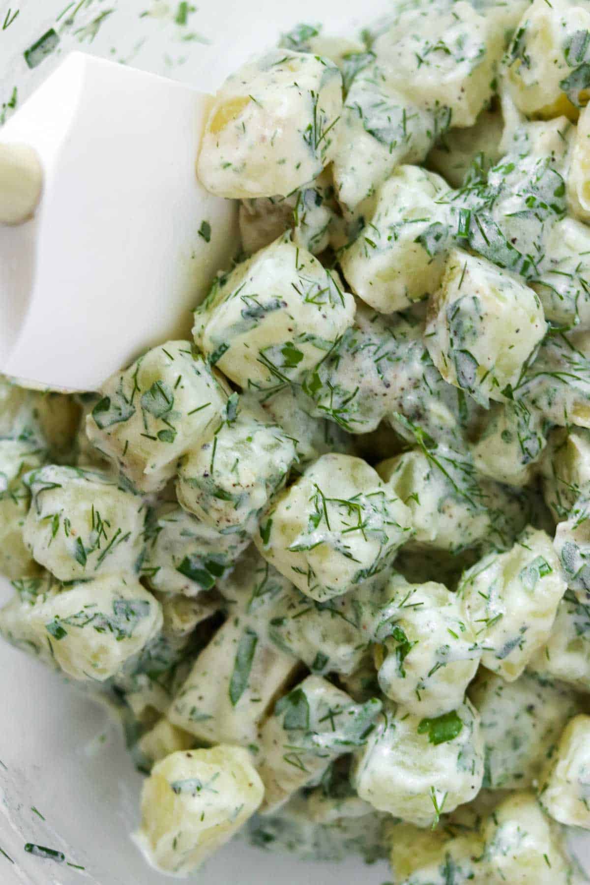 Rubber spatula stirring a creamy potato salad.