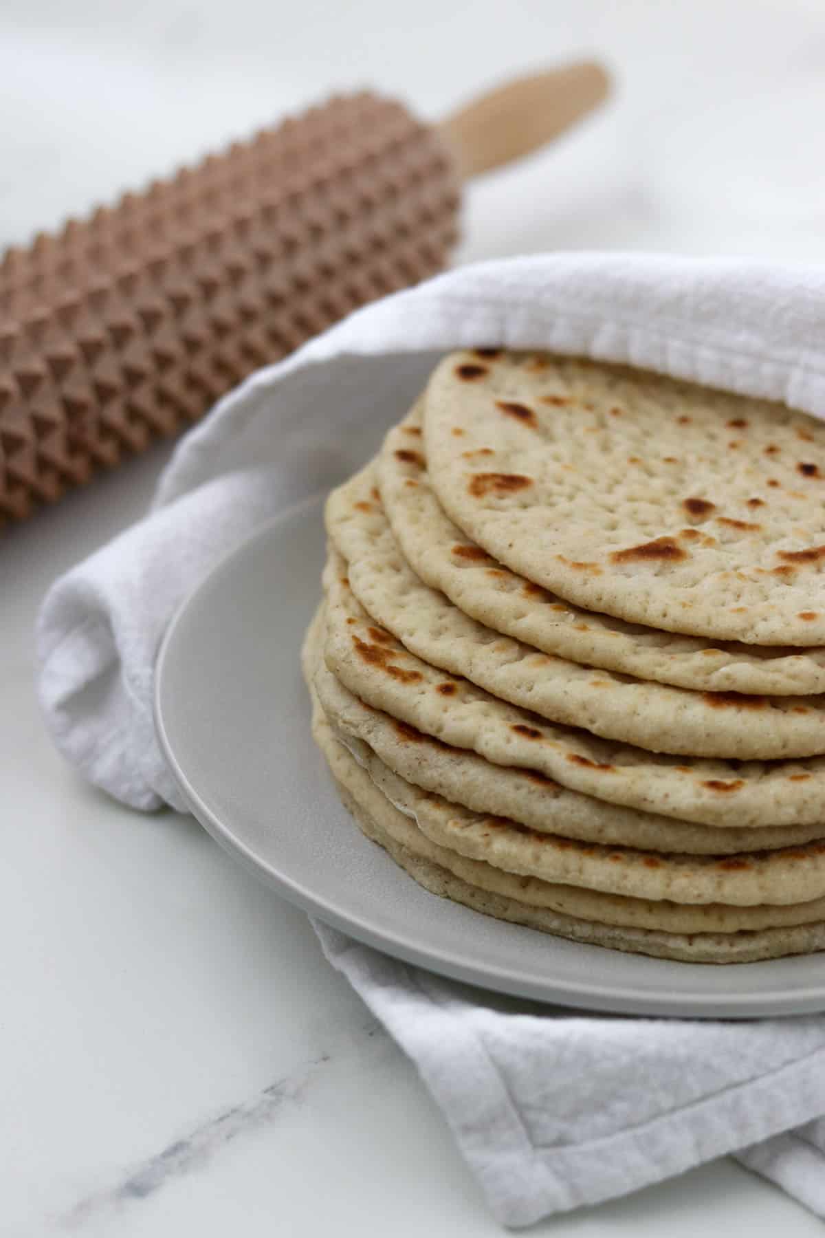 Soft Swedish Flatbreads on a plate next to a towel and a spiky rolling pin.