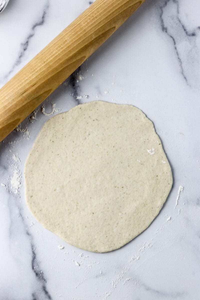 Flatbread dough rolled out on a marble counter with a rolling pin.