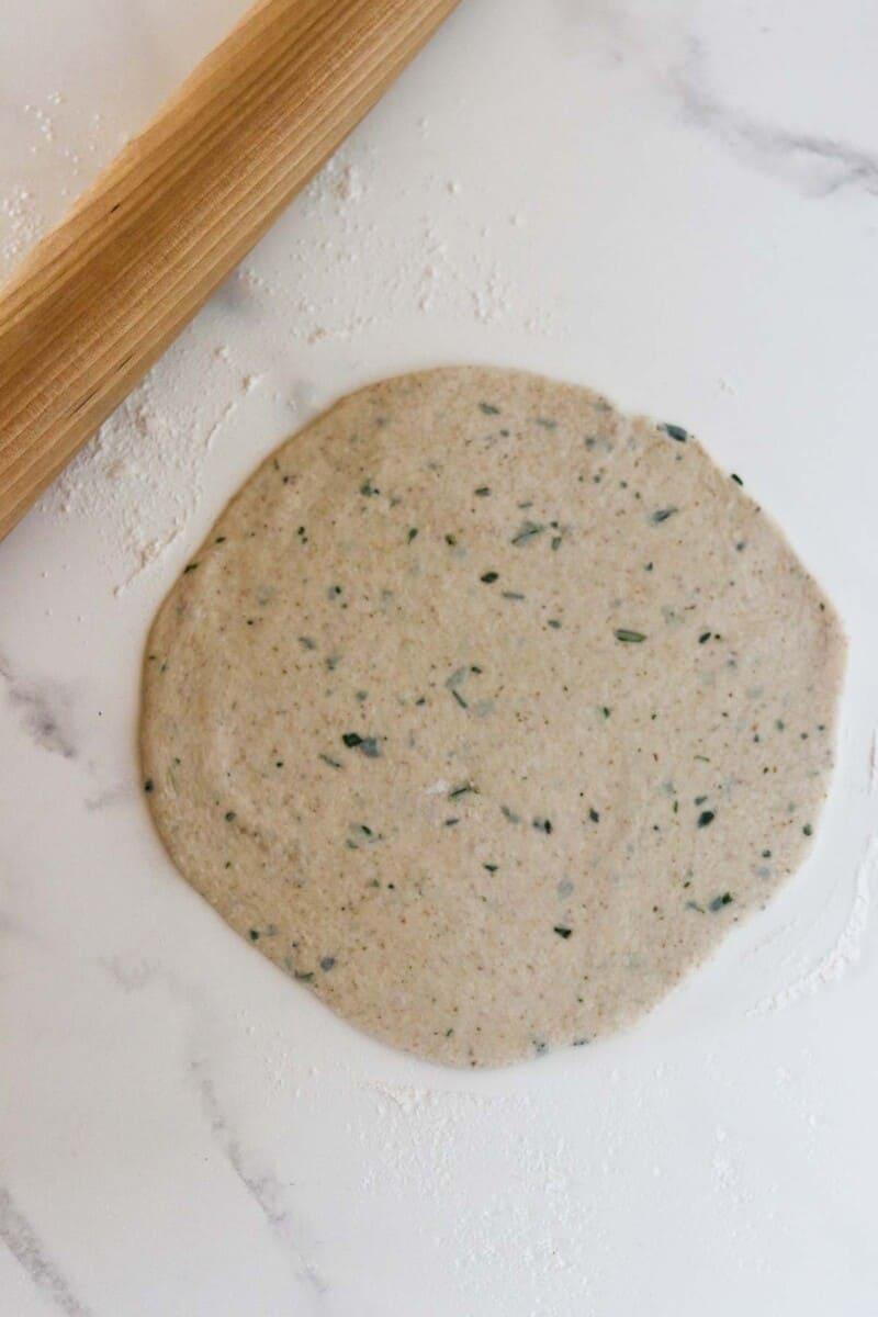 Rolled out flatbread dough next to a rolling pin.