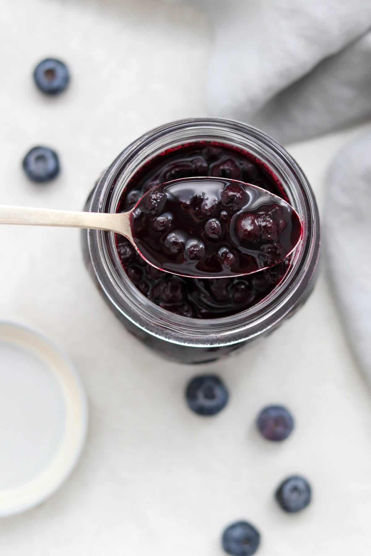 An overhead shot of a spoonful of blueberry cardamom compote resting over a jar.