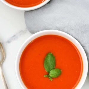 Two bowls of tomato red pepper soup topped with basil.