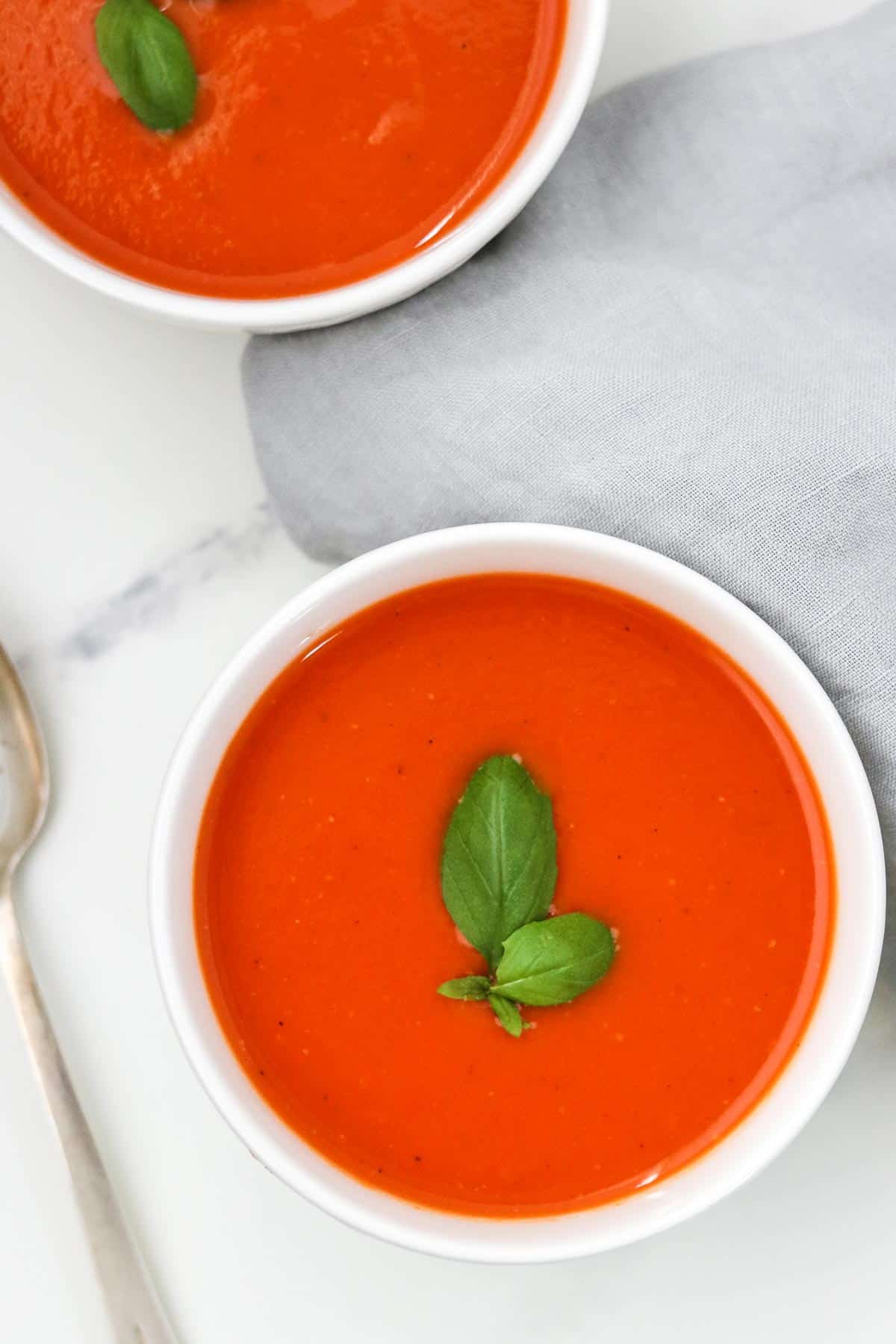 Two bowls of tomato red pepper soup topped with basil.