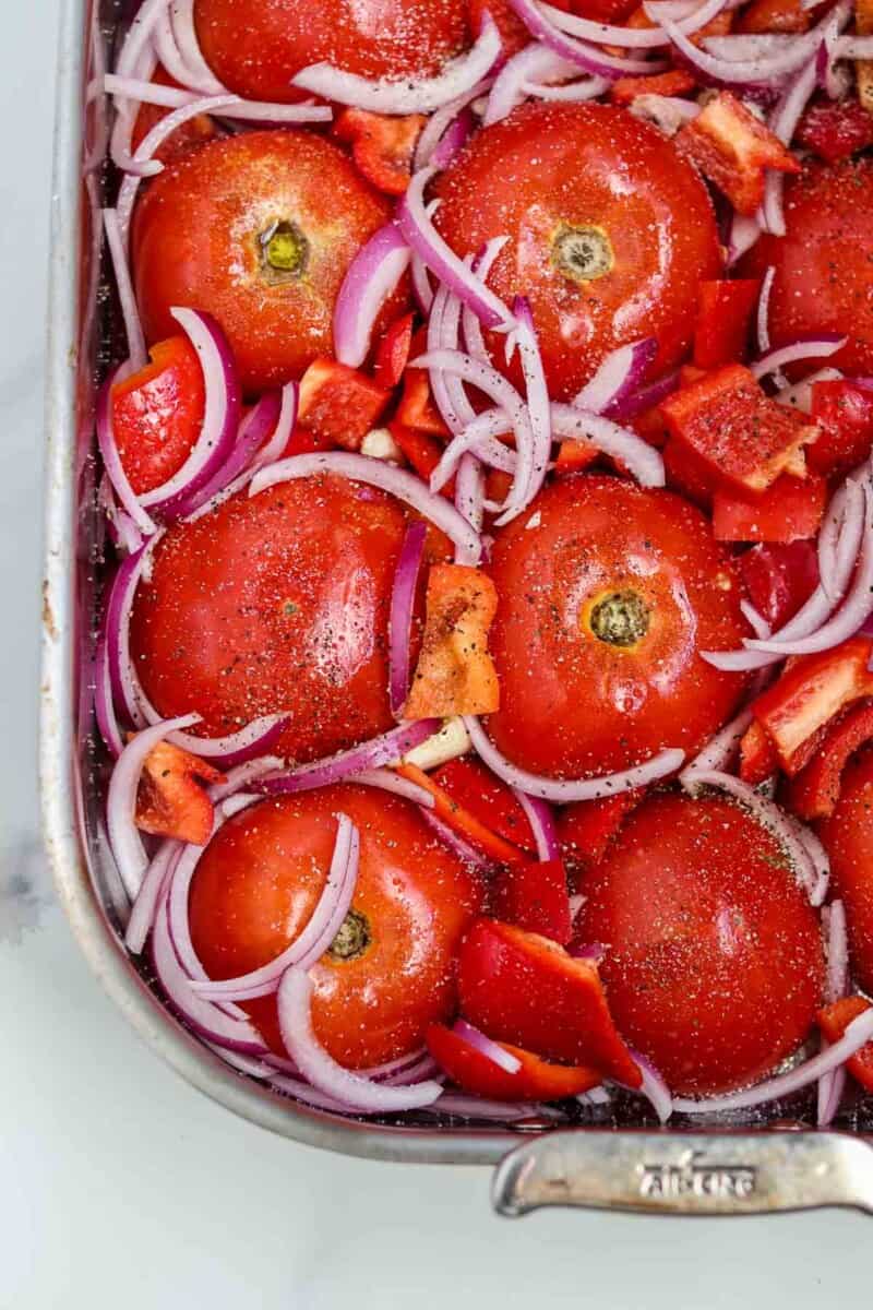 Tomato, red pepper and red onion in a roasting pan.