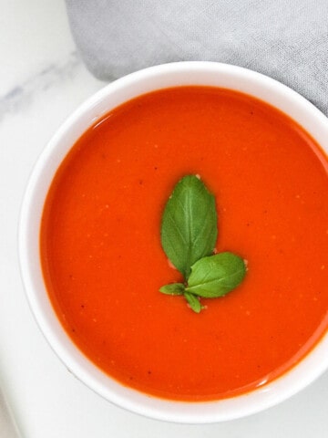 Bowl of roasted tomato red pepper soup topped with basil.