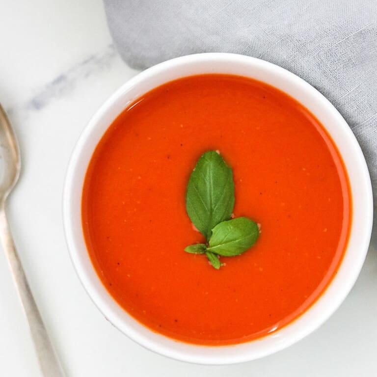 Bowl of roasted tomato red pepper soup topped with basil.