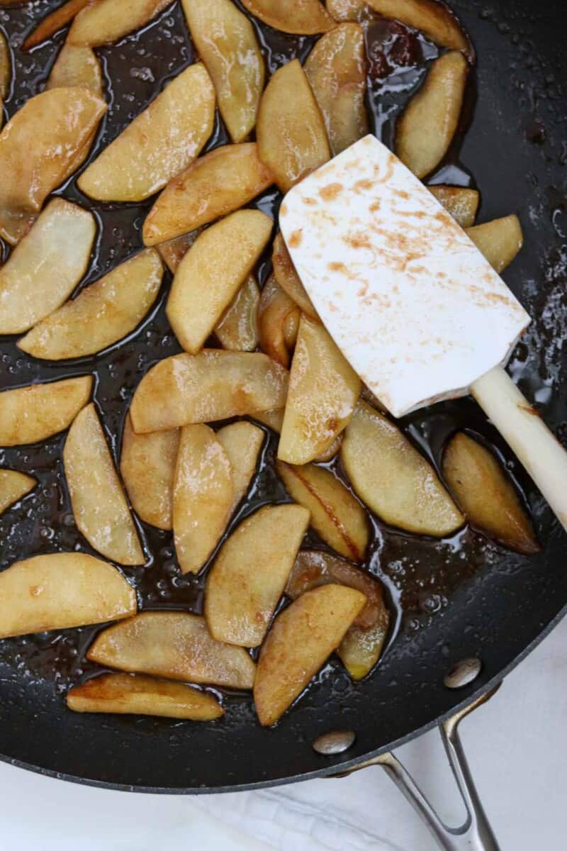 Cooked apple slices in a skillet with a rubber spatula.