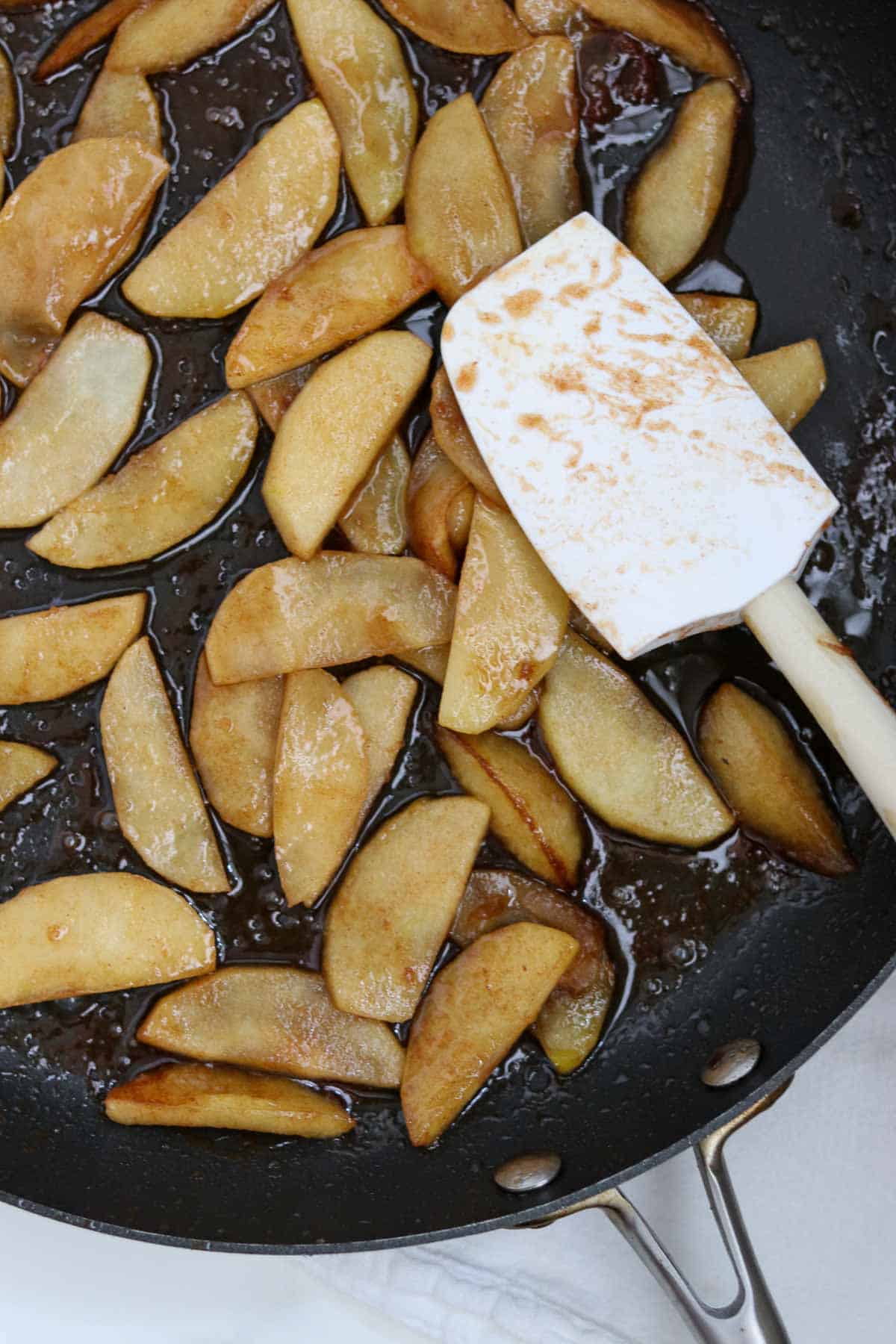 Cooked apple slices in a skillet with a rubber spatula.