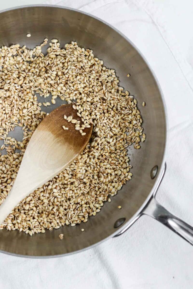 Barley grains in a saucepan with a wooden spoon.