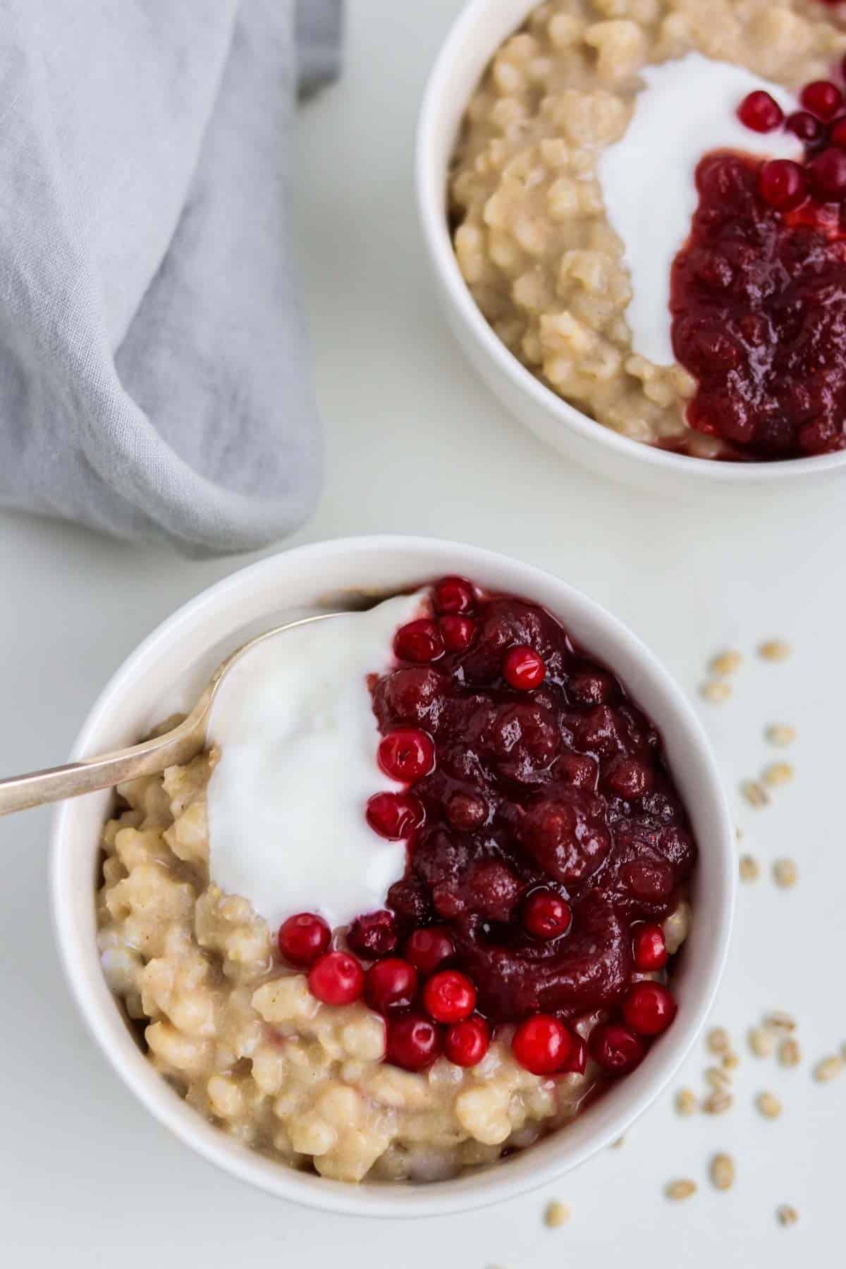 Overhead shot of a bowl of barley breakfast porridge topped with lingonberries and yogurt.