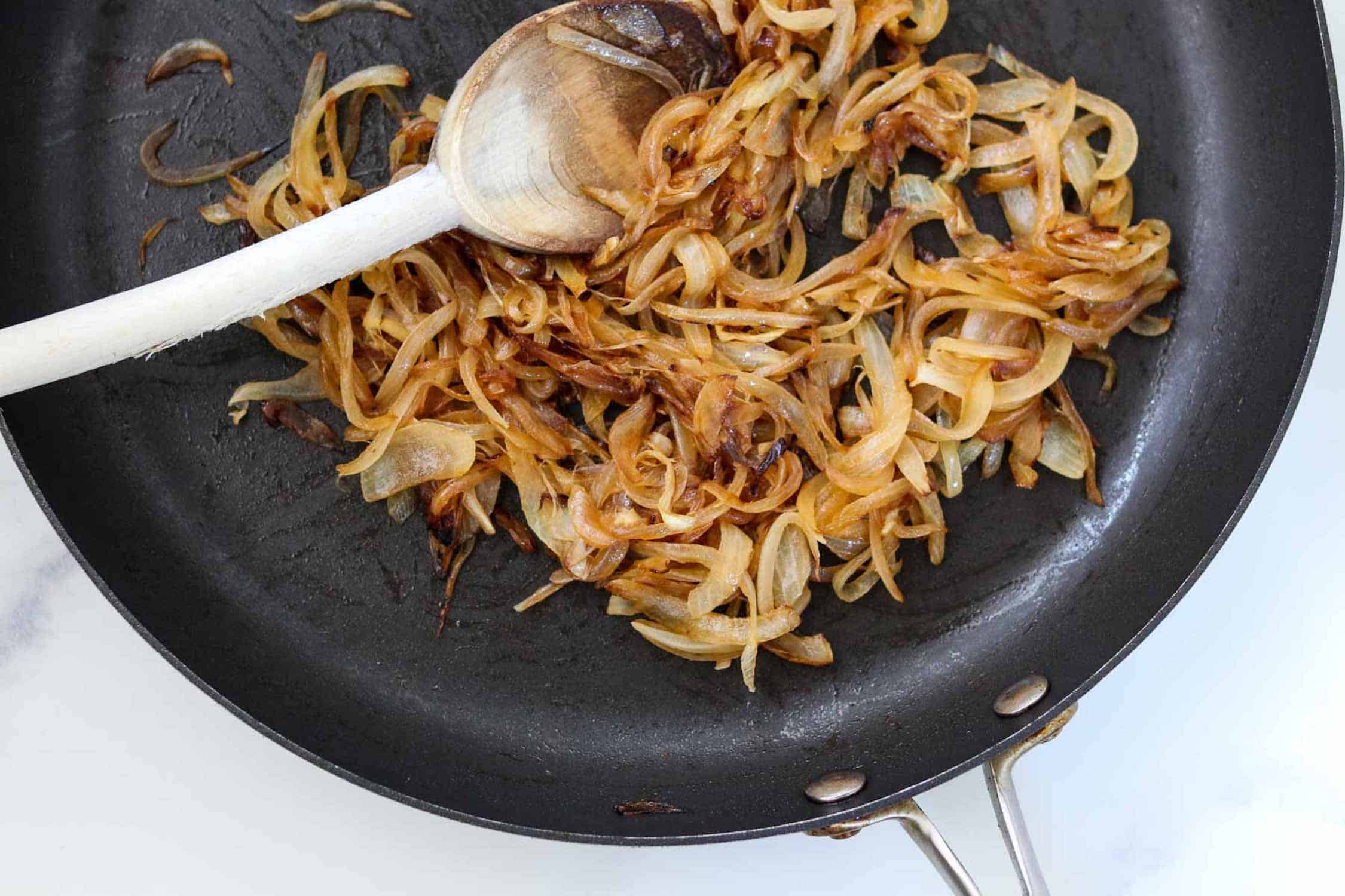 Caramelized onions in a pan with a wooden spoon.