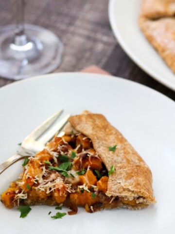 Slice of Butternut Squash Galette on a white plate next to a fork and glass of wine.