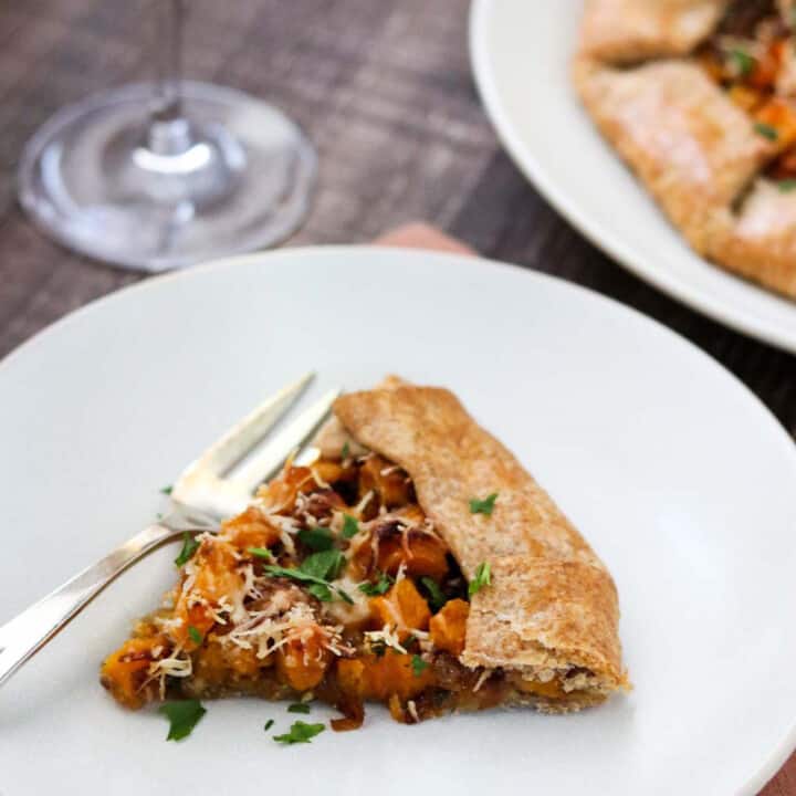 Slice of Butternut Squash Galette on a white plate next to a fork and glass of wine.