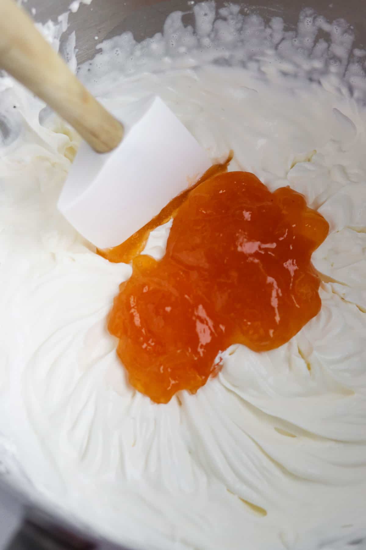 Cloudberry preserves on top of whipped cream in a metal bowl with a rubber spatula.