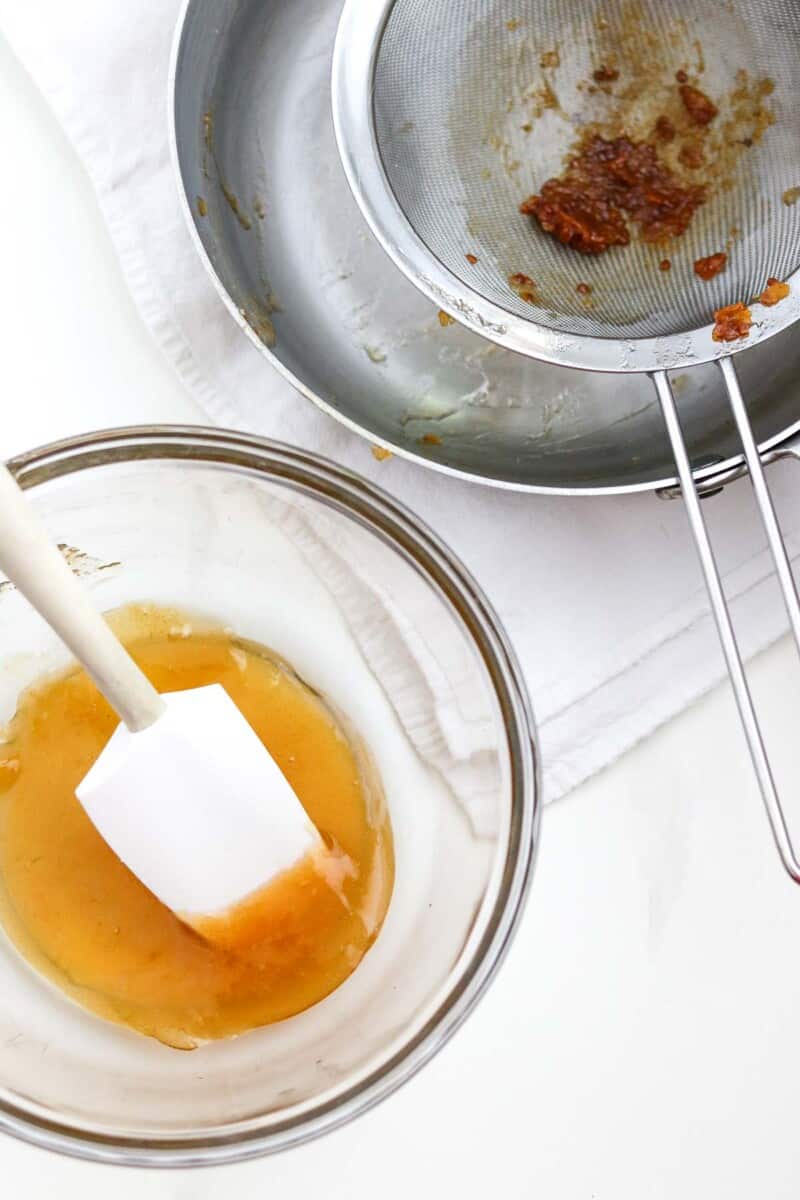 Strained cloudberry preserves in a glass bowl next to a strainer.