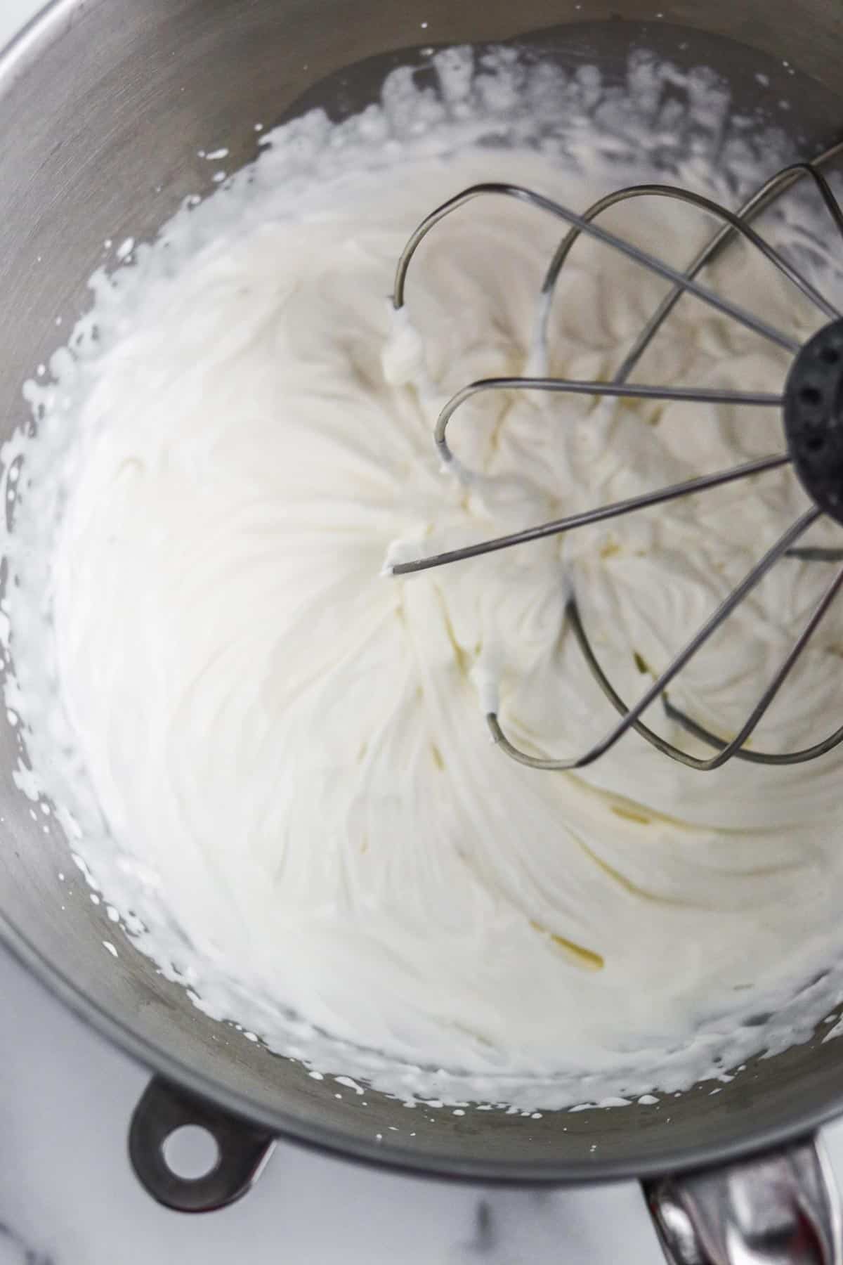 Whipped cream in a metal bowl with a whisk.
