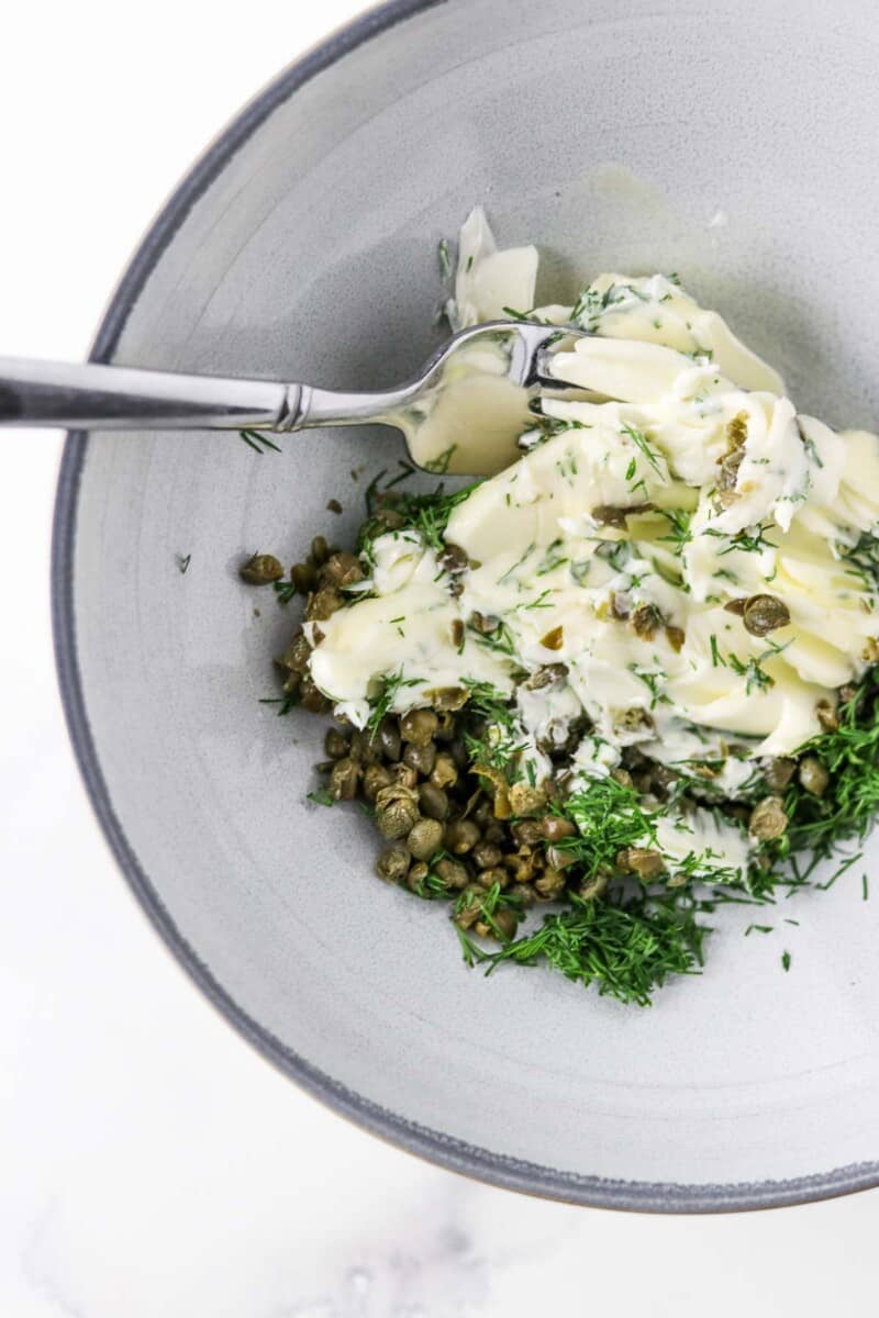 Butter, dill and capers together in a bowl with a fork.