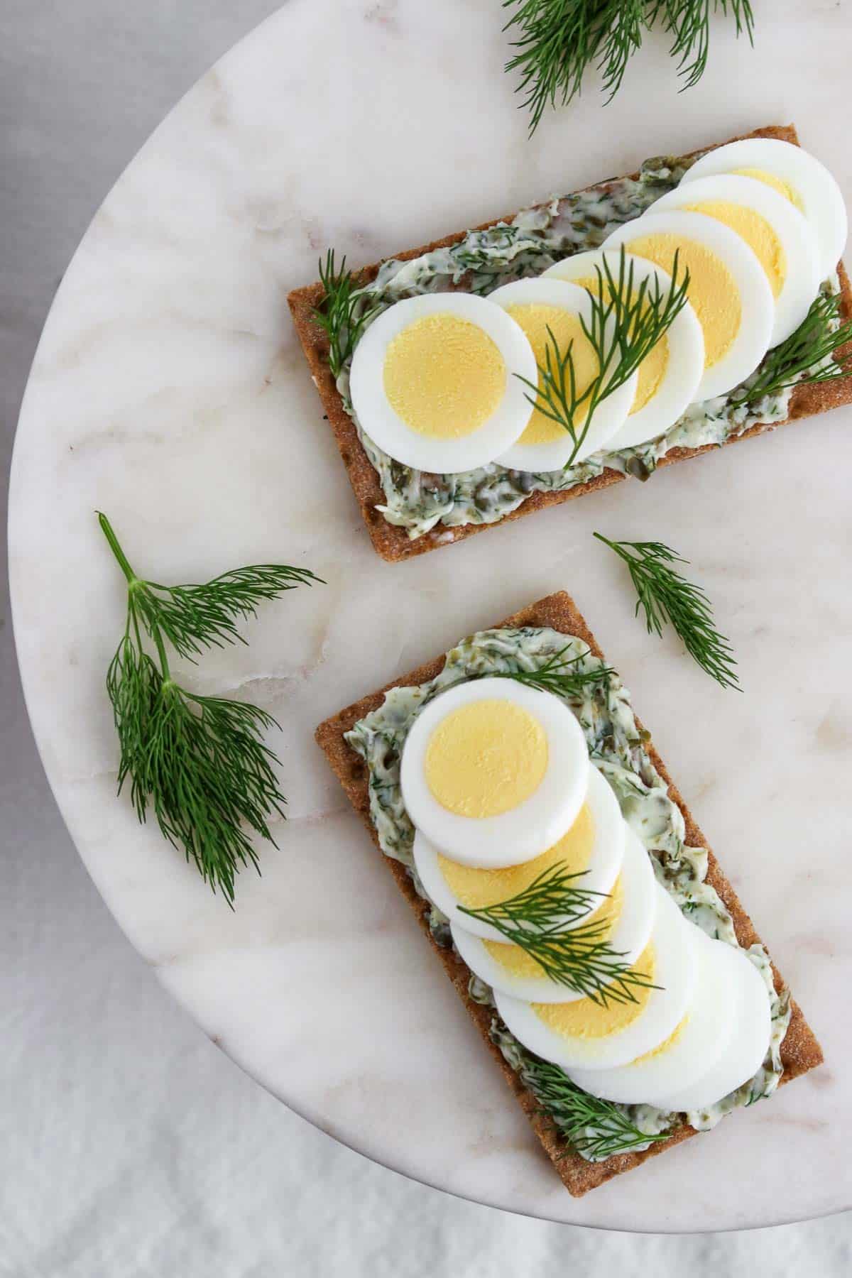 Overhead view of crispbread spread with dill caper butter and toped with hard-boiled egg and sprigs of dill.