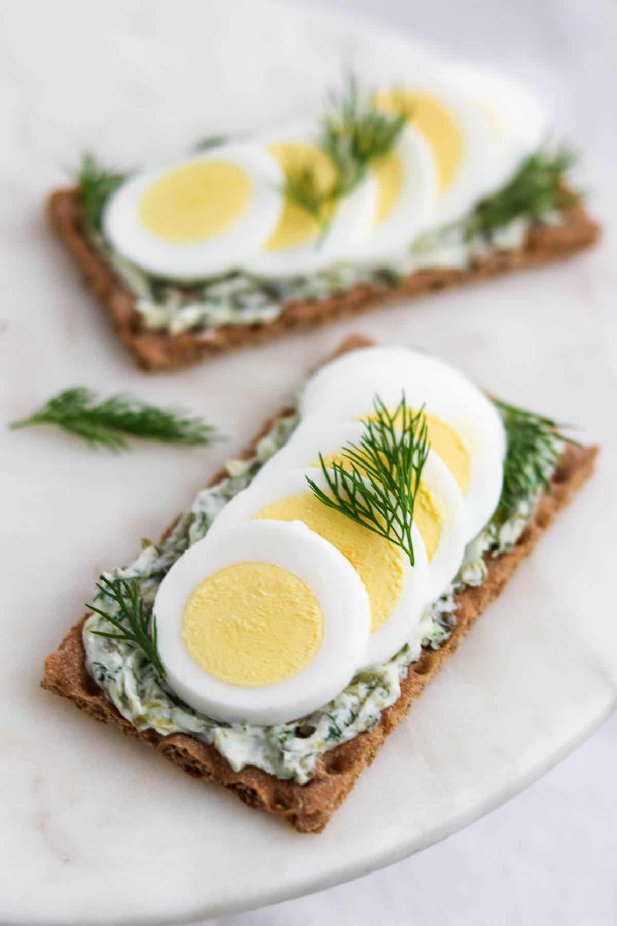 Crispbread topped with dill caper butter and slices of hard-boiled egg and dill sprigs.