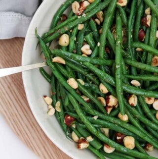 Green beans and hazelnuts in a bowl on a wood surface.