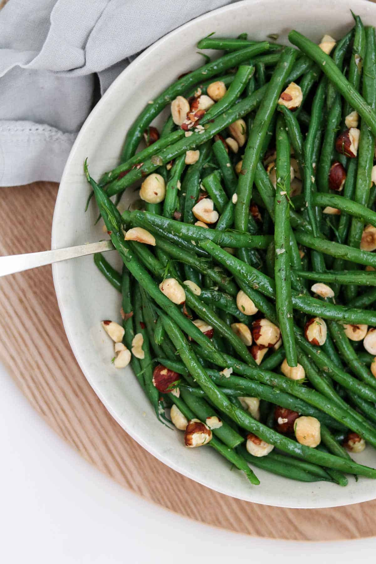 Green beans and hazelnuts in a bowl on a wood surface.