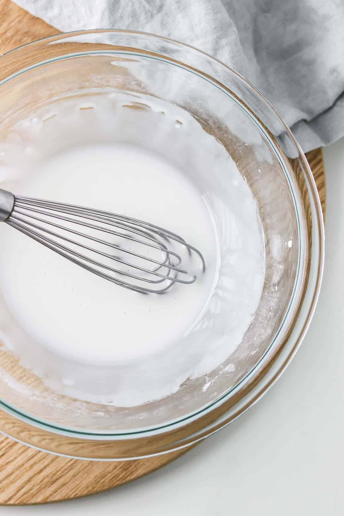 Powdered sugar glaze in a glass bowl with a whisk.