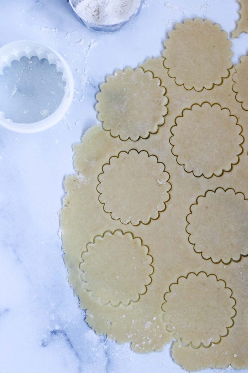 Cookie dough cut out into scalloped circle shapes on a marble surface.