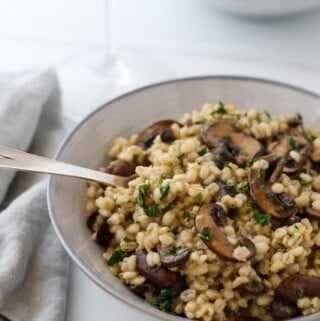 Creamy Baked Barley Risotto with Mushrooms in a bowl with a fork and a glass of wine.