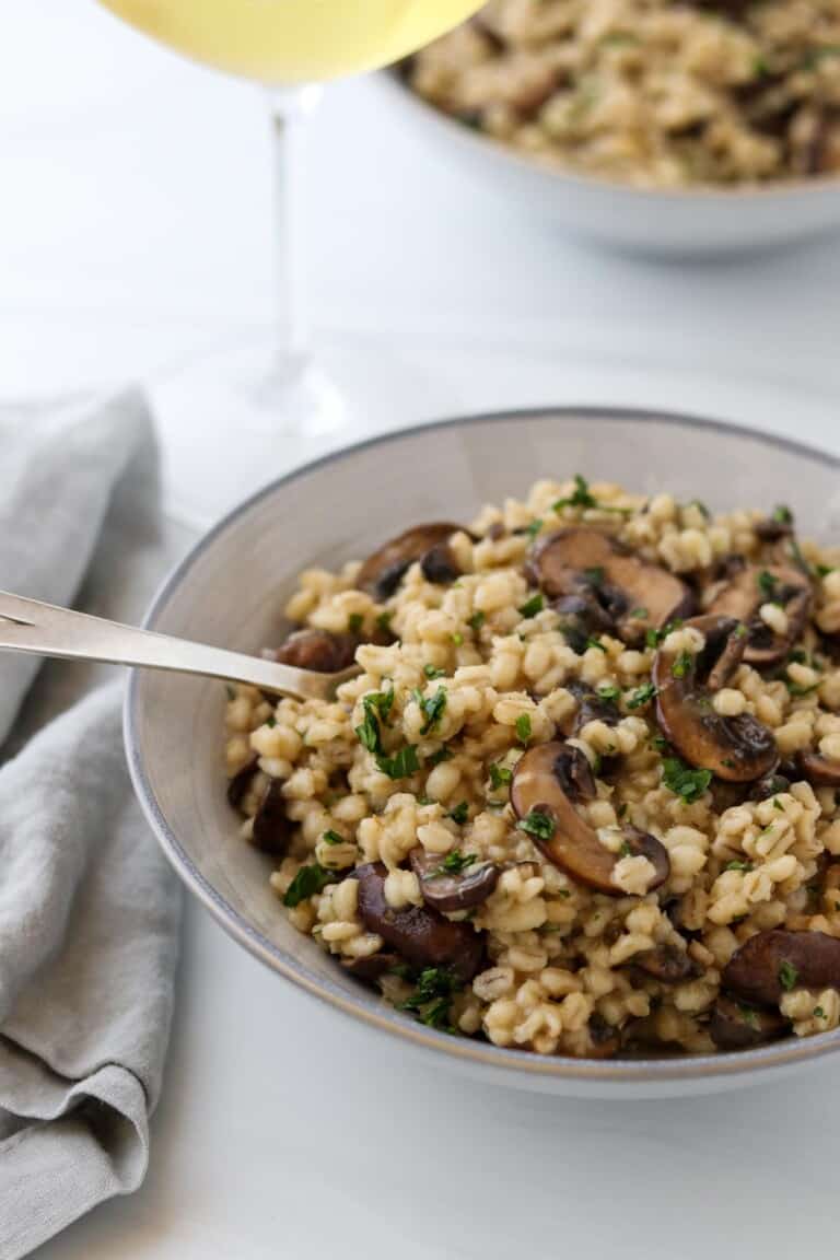 Creamy Baked Barley Risotto with Mushrooms in a bowl with a fork and a glass of wine.