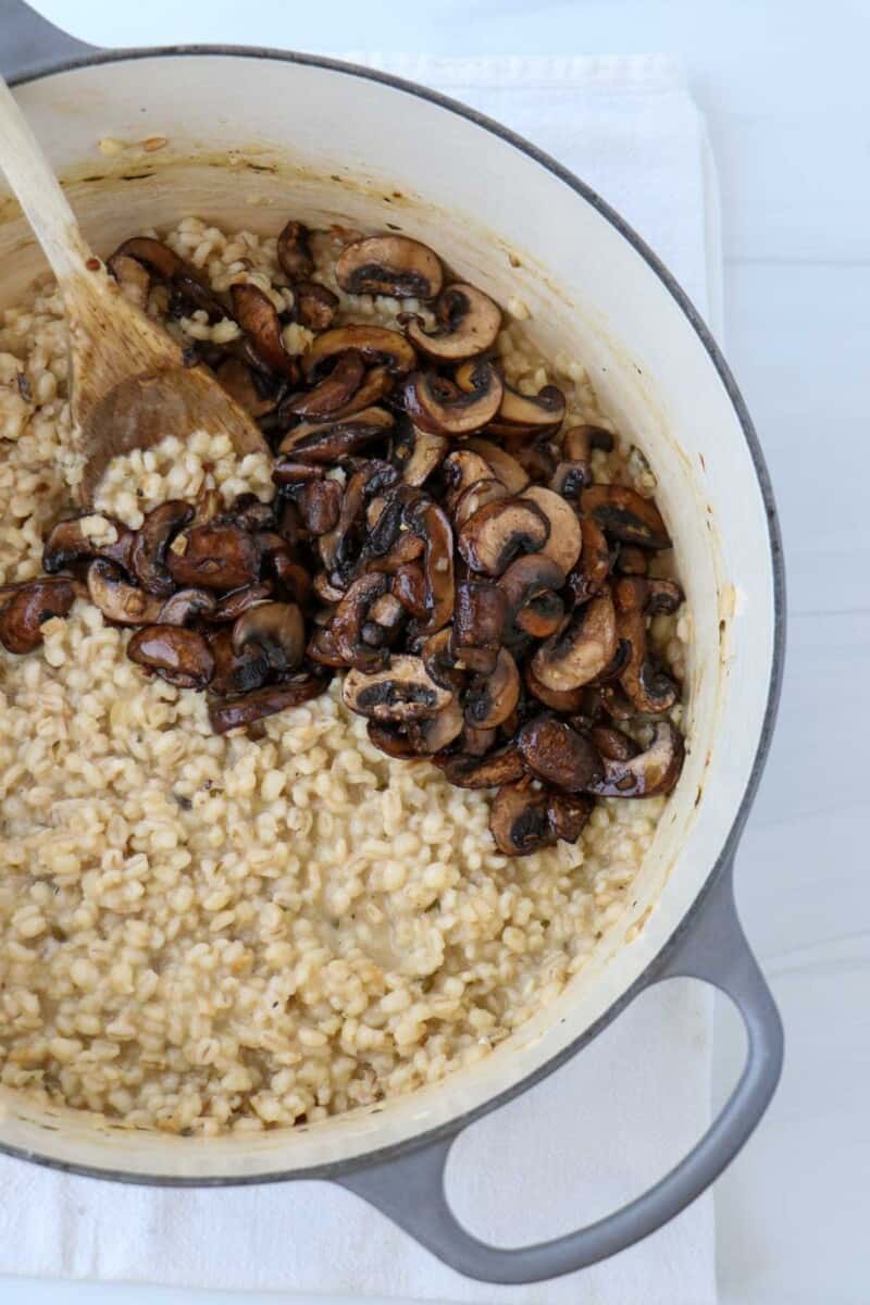 Barley risotto and mushrooms in a dutch oven with a wooden spoon.