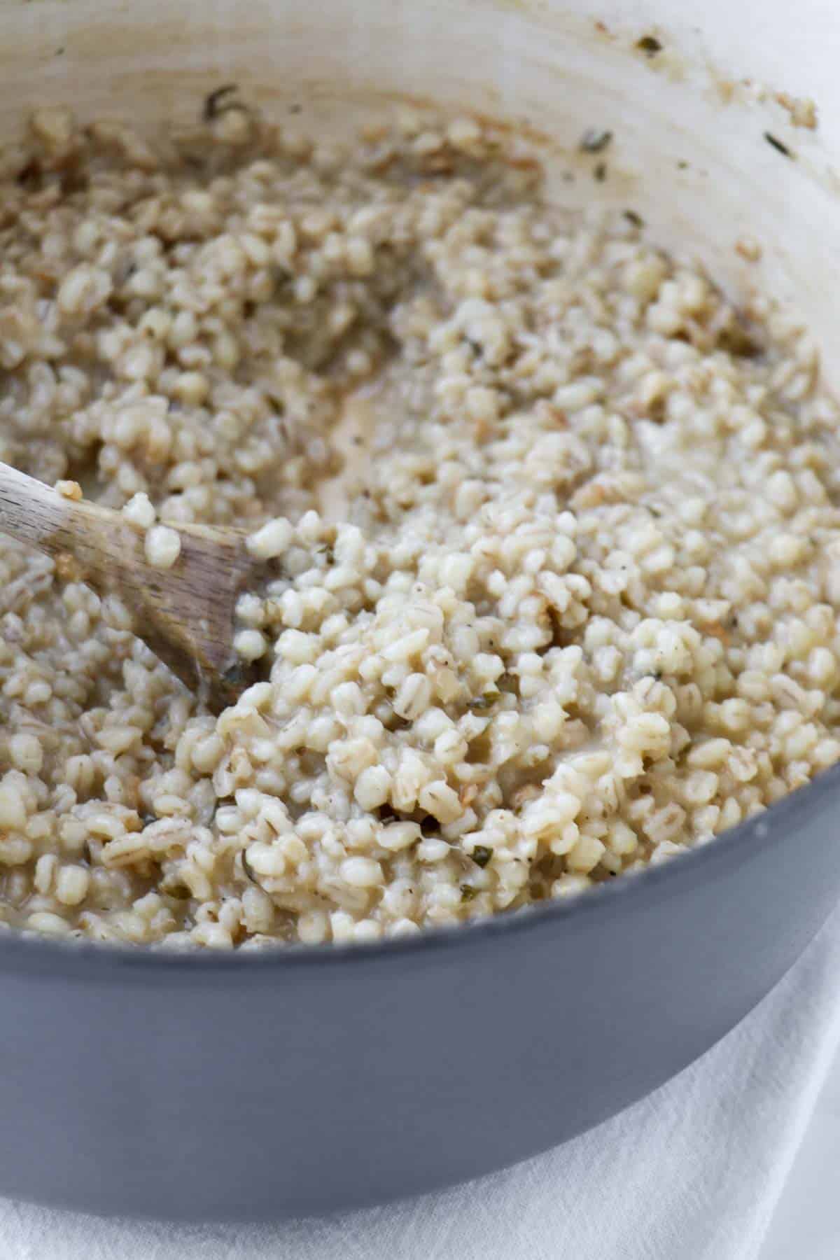 Creamy Baked Barley Risotto in a dutch oven with a wooden spoon.