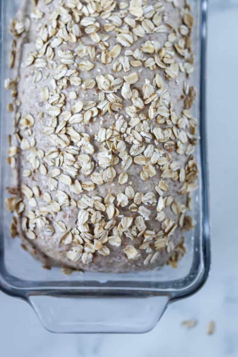 Unbaked bread dough topped with oats in a loaf pan.